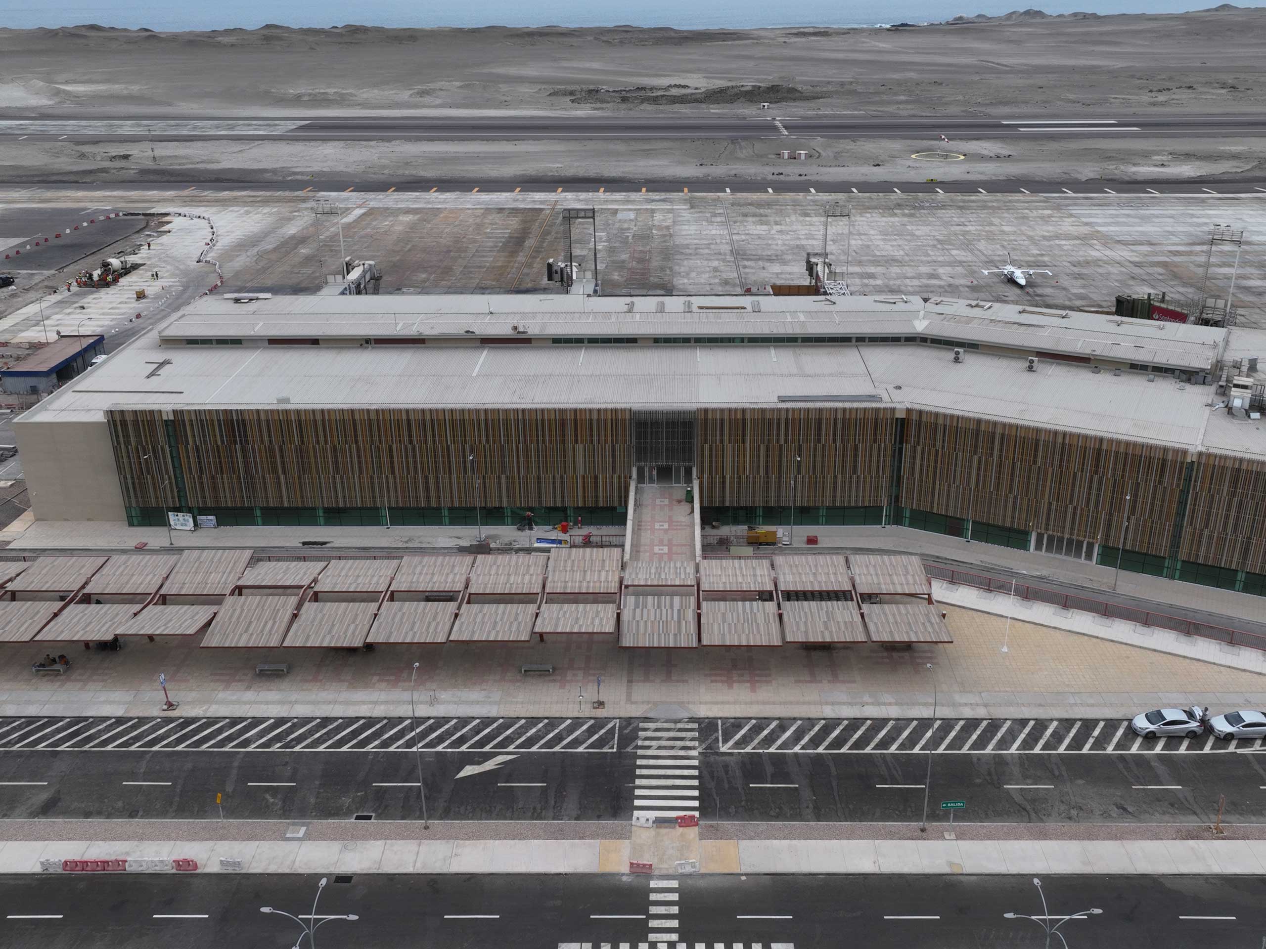 View of a bright, spacious terminal hall in Iquique Chile from 2023. The wide hall has high ceilings with visible steel beams, window fronts and escalators.